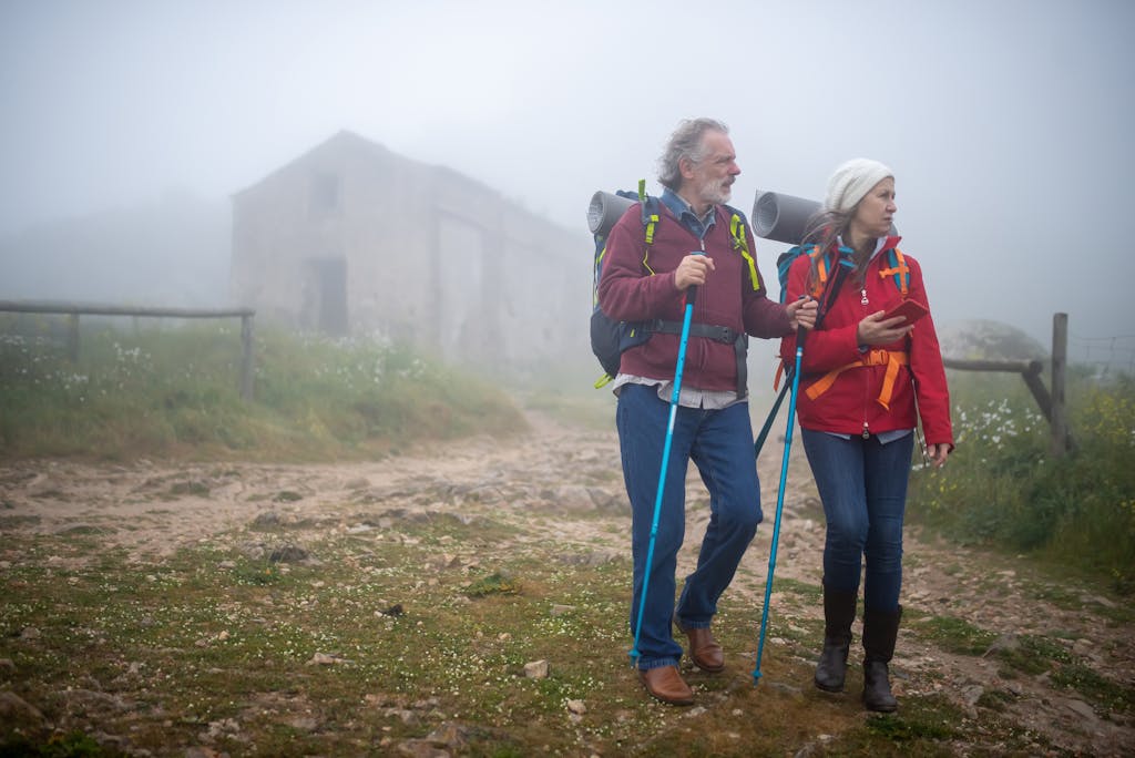 Elderly couple enjoying a foggy hike in rural Portugal, using trekking poles for support.